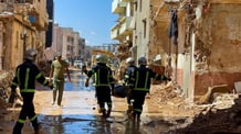Members of the rescue teams from the Egyptian army carry a dead body as they walk in the mud between the destroyed buildings, after a powerful storm and heavy rainfall hit Libya, in Derna